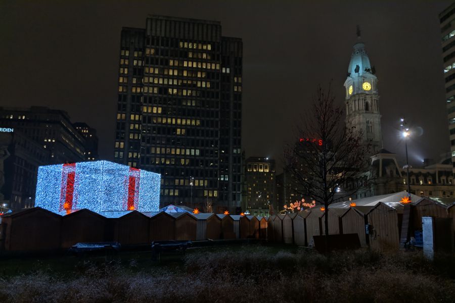 A giant illuminated present sits at the Philadelphia Christmas Market with City Hall in the background.