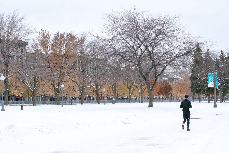 A jogger goes through the snow at Parc Lineaire de la Commune in Port Montreal with historic Old Montreal in the background.