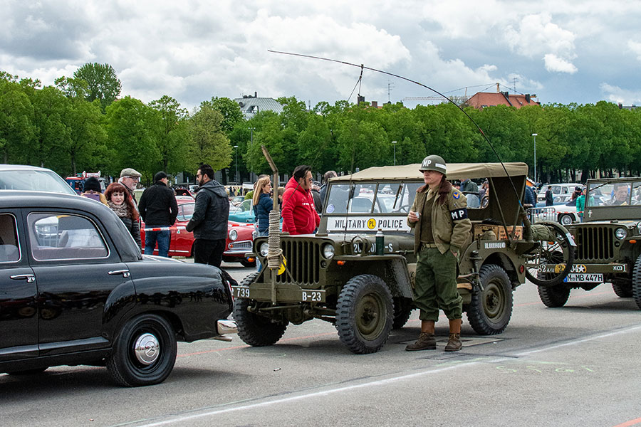 A man dressed as a military policeman stands outside of his military Jeep on the Wiesn at a Classic Car Show.