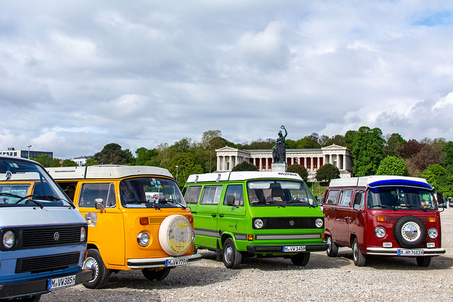 Four colorful VW Westfalia vans stand before the Bavaria statue on the Wiesn for the ACM Oldtimer-Treffen.