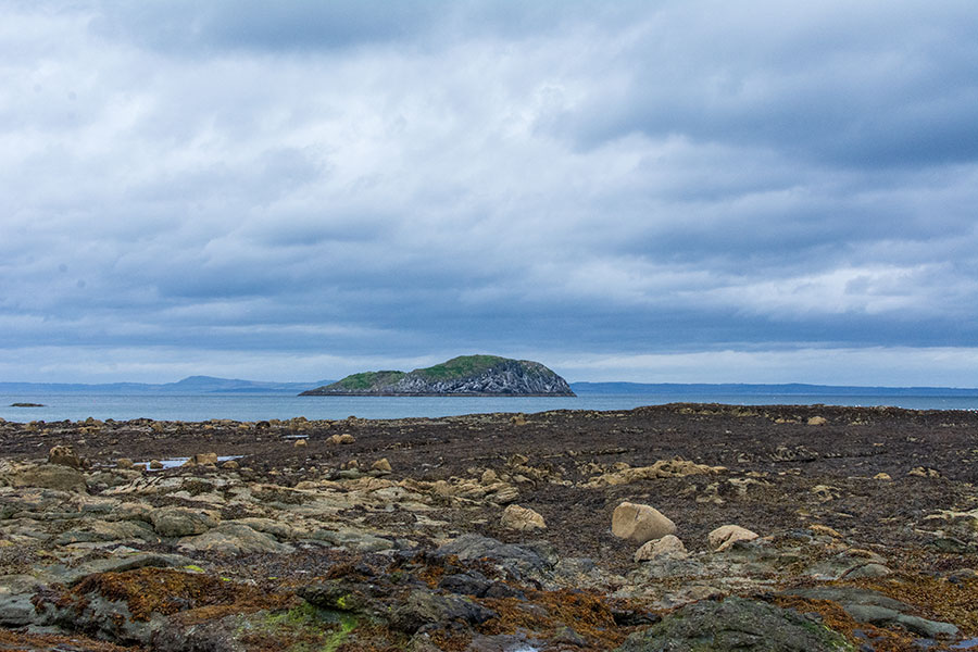 An island sits in the Firth of Forth in front of a stony beach in East Lothian.