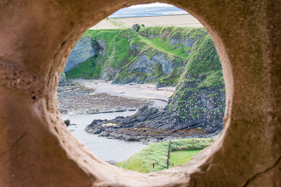 Looking through the stone at Tantallon Castle, birds fly along the cliffs.