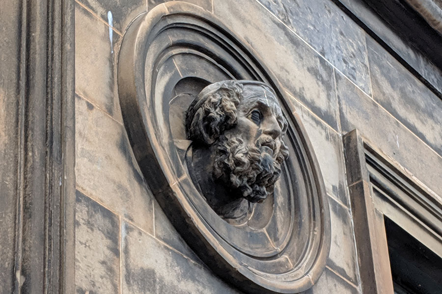 A stone head peeks out of an architectural detail on a building in Glasgow.