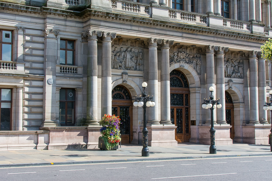 Vintage light posts and flowers sit in front of the highly decorated Glasgow City Chambers entrance.