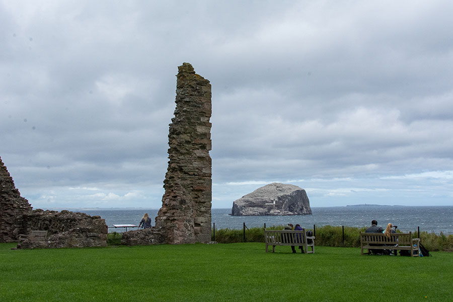 Visitors sit on benches in the courtyard at Tantallon Castle, looking onto Bass Rock, near the remains of its curtain wall.