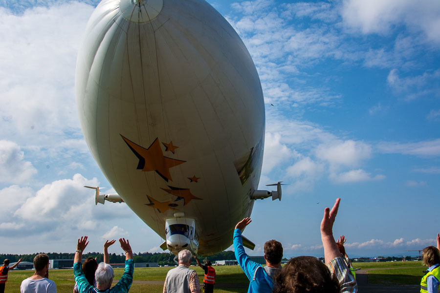 Passengers wave as the Zeppelin NT airship takes off.