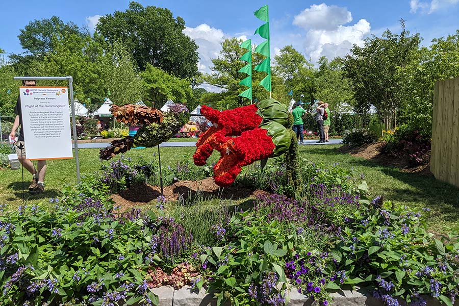 Flower arrangements create a larger-than-life hummingbird gathering nectar.