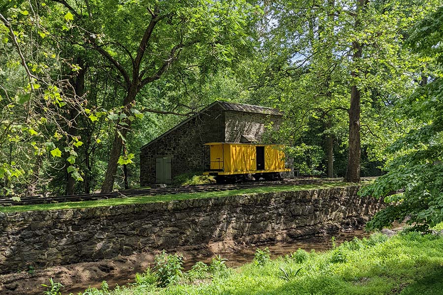 A yellow train car sits on the rails along the Brandywine River at the power yards of Hagley Museum and Library.