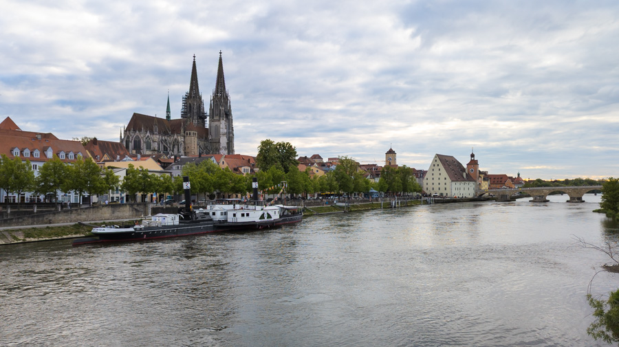 A ferry docked on the Danube River in front of the Regensburg skyline, with the cathedral.