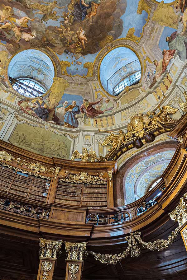 Ceiling frescoes flow down on the walls of the second floor of the State Hall of the Austrian National Library.