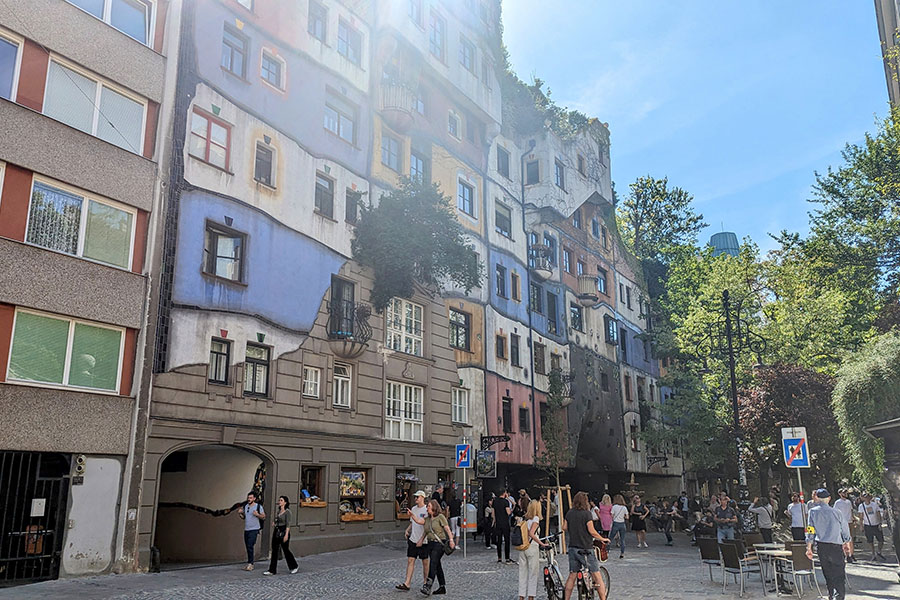 Wide-angle view of Hundertwasserhaus, a colorful residential building with lush greenery growing on the roof.