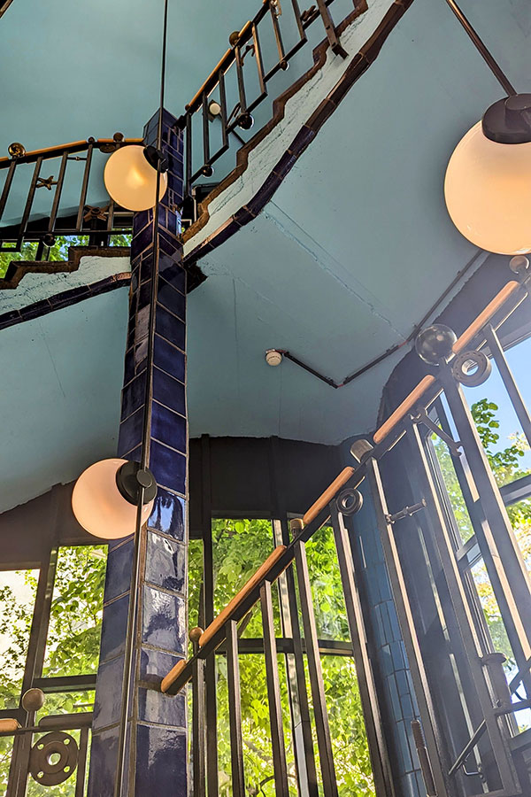 Interior stairwell of KunstHausWien, showcasing Hundertwasser's artistic design with curved lines, blue tiles, and natural light.